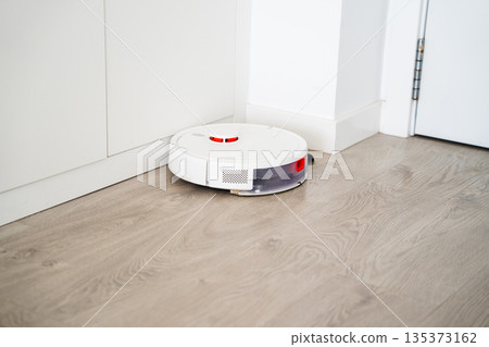 Automatic robot vacuum cleaner cleaning hard floor under kitchen cabinets with smart navigation and modern home automation Automatic robot vacuum cleaner cleaning hard floor under kitchen cabinets with smart navigation and modern home automation 135373162