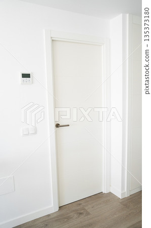 Minimal white interior door with wall thermostat and light switches, bright modern apartment hallway with wood floor and copy space Minimal white interior door with wall thermostat and light switches, bright modern apartment hallway with wood floor and copy space 135373180