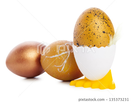 Golden eggs in egg holder with two brown eggs in background on white surface 135373231