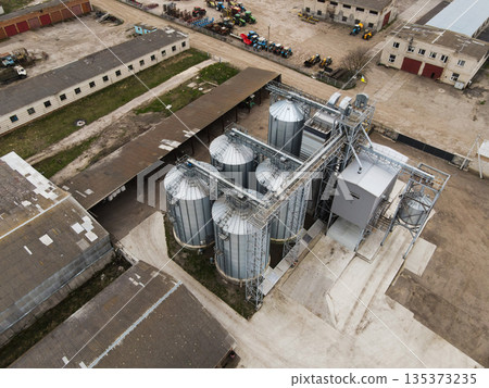 Aerial drone shot of industrial farm grain facility with metal storage silos, conveyor system and warehouse roofs, rural logistics Aerial drone shot of industrial farm grain facility with metal storage silos, conveyor system and warehouse roofs, rural logistics 135373235