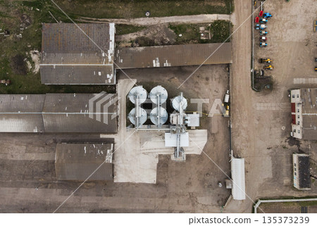 Top-down drone view of agricultural grain elevator with storage silos, conveyors and warehouses in an industrial farm complex 135373239