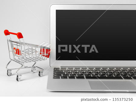Shopping cart next to a laptop for online shopping at home Shopping cart next to a laptop for online shopping at home 135373250
