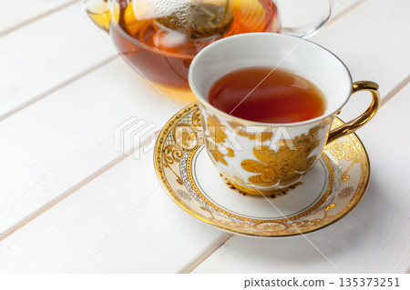 Enjoying tea from a fine cup and saucer with a teapot in the background Enjoying tea from a fine cup and saucer with a teapot in the background 135373251