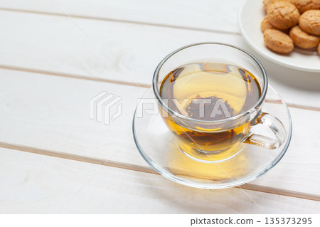 Warm tea in a glass cup with cookies on a white table during a cozy afternoon 135373295