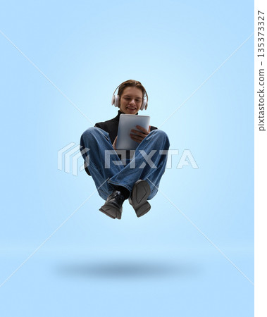 Casual man levitating with tablet and headphones on blue background. Casual man levitating with tablet and headphones on blue background. 135373327
