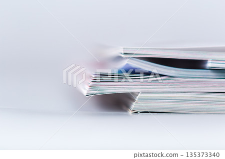 Stacked magazines resting on a white surface with blurred background in a simple setup 135373340