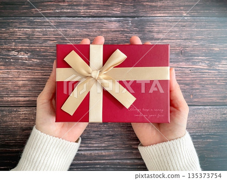 Woman's hand holding a red gift box on a wooden table Woman's hand holding a red gift box on a wooden table 135373754