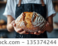 A female baker holds freshly baked country bread in her hands. 135374244