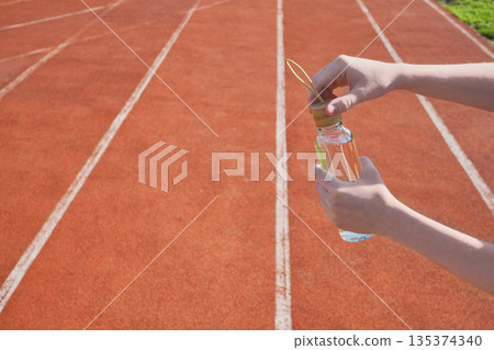 Athlete's hands prepare bottle of water for refreshment on red running track 135374340