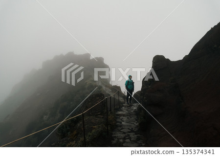An individual confidently traverses cloudcovered mountain ridge An individual confidently traverses cloudcovered mountain ridge 135374341