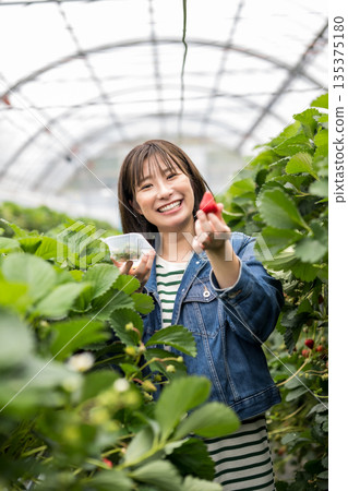 A woman holding a strawberry with a smile 135375180