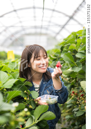 A woman holding a strawberry with a smile 135375182