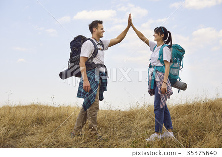 Hikers couple high-fiving on forest trail, smiling with backpacks and gear Hikers couple high-fiving on forest trail, smiling with backpacks and gear 135375640