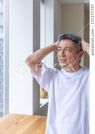 Senior man holding his head by the window 135375787