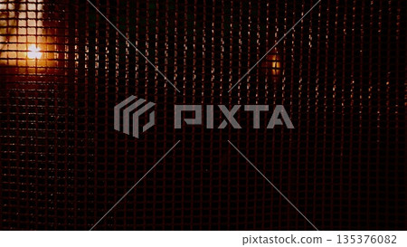 vibrant sunset rays piercing dark chain link fence mesh in urban twilight evoking mystery and intrigue for atmospheric wallpaper or banner with copy space 135376082