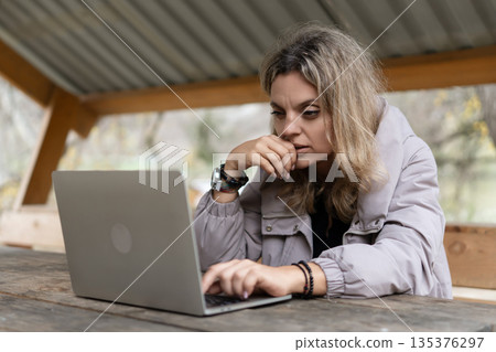Woman working laptop concentrating on remote business outdoors at wooden table Woman working laptop concentrating on remote business outdoors at wooden table 135376297