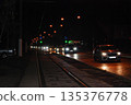 Nighttime city street with cars and tram trackst.  Nighttime city street featuring multiple cars driving along a road with tram tracks visible beside them. 135376778