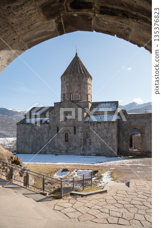 View of the Cathedral of Saints Paul and Peter framed by a stone archway, conical dome, arched narthex entrance, snow-covered courtyard 135376823