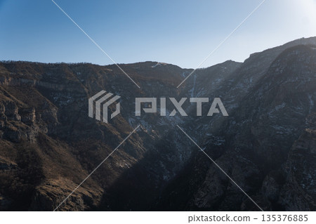 Mountain gorge landscape in Armenia shows steep rocky slopes with light snow patches, deep shadows, dramatic natural relief Mountain gorge landscape in Armenia shows steep rocky slopes with light snow patches, deep shadows, dramatic natural relief 135376885