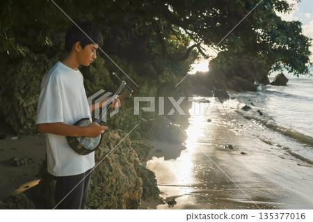 A boy playing the sanshin on the beach 135377016