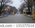 Long view of a cobblestone city street with pedestrians and sculptures. Cobblestone street lined with leafless trees and classic street lamps in Odessa.  135377018