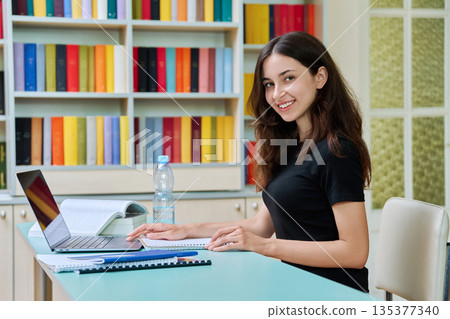 Portrait of teenage student girl studies in the library with laptop and books Portrait of teenage student girl studies in the library with laptop and books 135377340