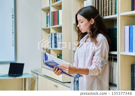 Portrait of teenage beautiful girl high school student reading textbook in library classroom 135377348