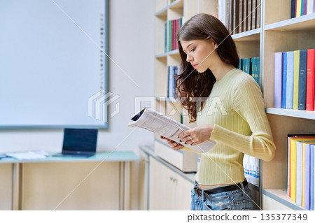Portrait of teenage beautiful girl high school student reading textbook in library classroom 135377349