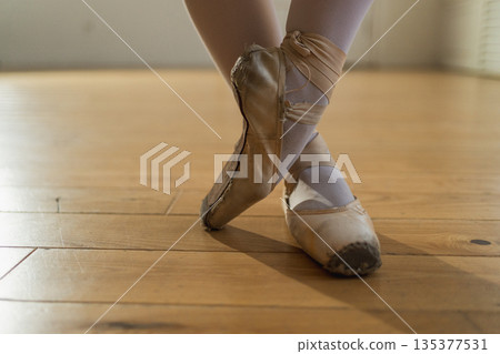 Worn ballet pointe shoes on feet in dance class. Well worn pointe shoes of ballet dancer. Classical ballerina woman in dance studio. Classical pointe shoes for dance training. Ballet school concept Worn ballet pointe shoes on feet in dance class. Well worn pointe shoes of ballet dancer. Classical ballerina woman in dance studio. Classical pointe shoes for dance training. Ballet school concept 135377531