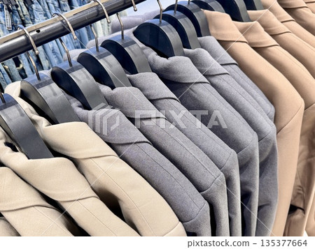 New stylish classic cut jackets in pastel shades are hanging on hangers in a clothing store. High quality photo 135377664