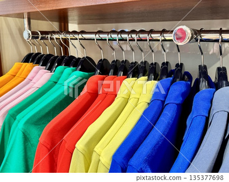 Stylish luxury men's clothing store, new colorful cotton polos hanging on hangers in the store 135377698