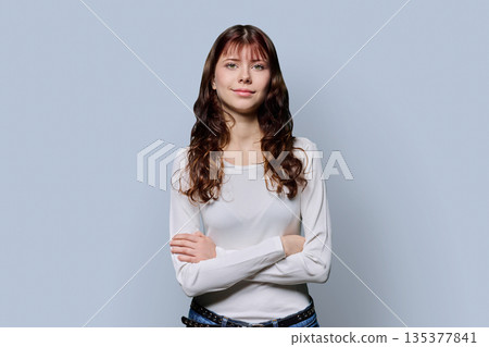 Portrait of smiling confident teenage girl with crossed arms on light background 135377841