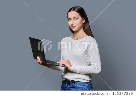 Portrait of smiling teenage girl holding laptop on gray studio background Portrait of smiling teenage girl holding laptop on gray studio background 135377859