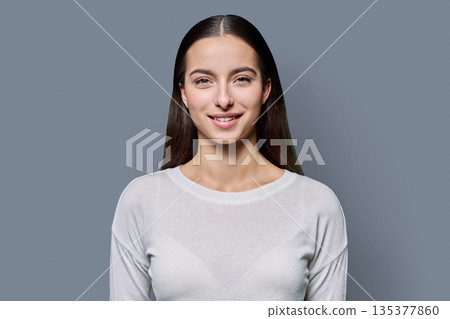 Portrait of beautiful smiling teenage woman against gray studio background Portrait of beautiful smiling teenage woman against gray studio background 135377860