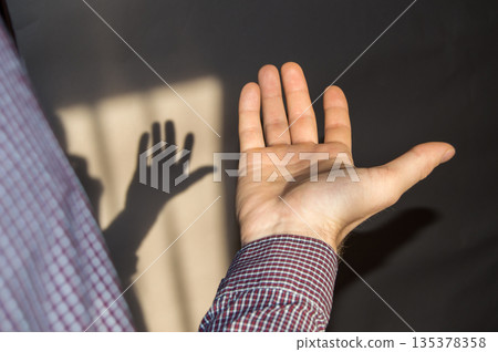 The young man holds an empty hand with his palm up, a shadow on the wall 135378358