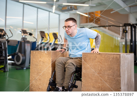 Dedicated disabled man with spinal injury working on arms and upper body strength on wooden blocks. 135378897