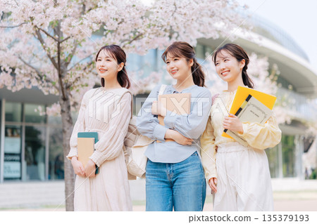 三位女大學生漫步在櫻花盛開的校園裡。 135379193