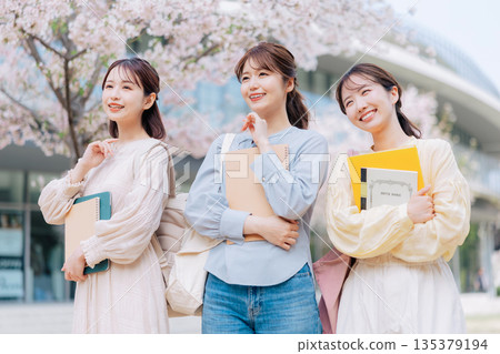 三位女大學生漫步在櫻花盛開的校園裡。 135379194