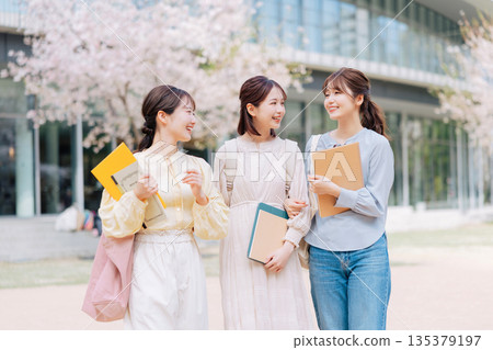 三位女大學生漫步在櫻花盛開的校園裡。 135379197