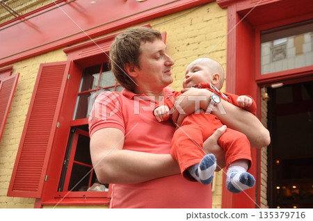 Father Holding Baby in Matching Red Outfits Outdoors 135379716