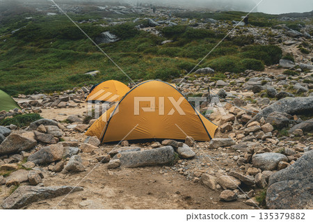 Tents pitched at a foggy alpine campsite and hiking trails Tents pitched at a foggy alpine campsite and hiking trails 135379882