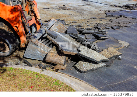 Heavy machinery is lifting removing broken asphalt pieces from construction site Heavy machinery is lifting removing broken asphalt pieces from construction site 135379955
