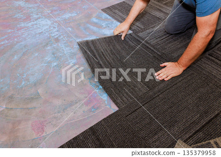 Worker carefully positions flooring carpet tiles in home improvement task to interior space. 135379958