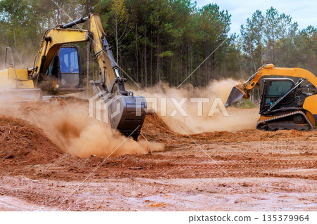 Heavy bulldozer equipment excavator clears land on construction site, creating dust preparing for future building Heavy bulldozer equipment excavator clears land on construction site, creating dust preparing for future building 135379964