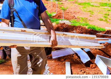 Man holds wooden beams while working at construction site soil building materials are around. 135379989