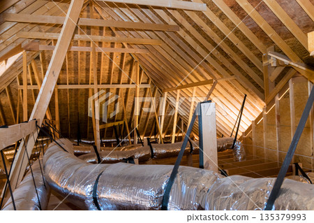 Ductwork wooden structure are visible in spacious attic, with sunlight shining through rafters. Ductwork wooden structure are visible in spacious attic, with sunlight shining through rafters. 135379993