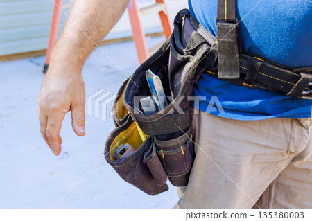 Construction worker tool belt filled with tools while working on site in busy construction area. Construction worker tool belt filled with tools while working on site in busy construction area. 135380003