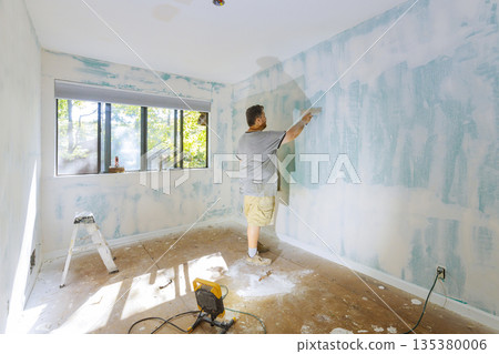 Worker is applying putty plaster to walls of room with windows surrounded by tools dust. Worker is applying putty plaster to walls of room with windows surrounded by tools dust. 135380006
