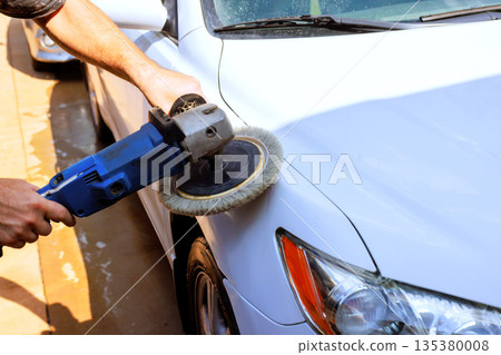 Service worker is polishing white car using power buffer in ensuring shiny finish. 135380008