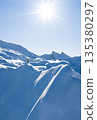 Freeride skier standing on a snowy mountain ridge, preparing for descent in pristine alpine terrain. Bright winter sun, dramatic peaks and untouched snow create a powerful adventure atmosphere. 135380297